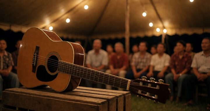 Gitar akustik di atas peti kayu di tenda pentas desa dengan penonton duduk menonton